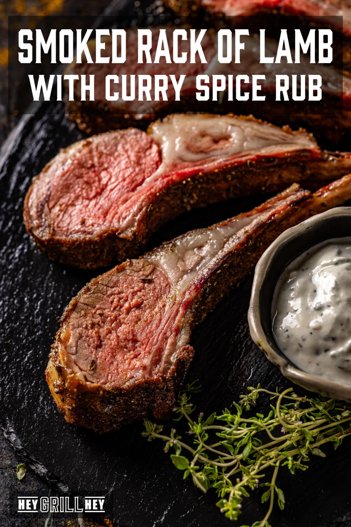 Bone-in sliced lamb on a plate with bowl of white sauce. The text overlay reads "Smoked Rack of Lamb with Curry Spice Rub" at the top, and "Hey Grill Hey" at the bottom.