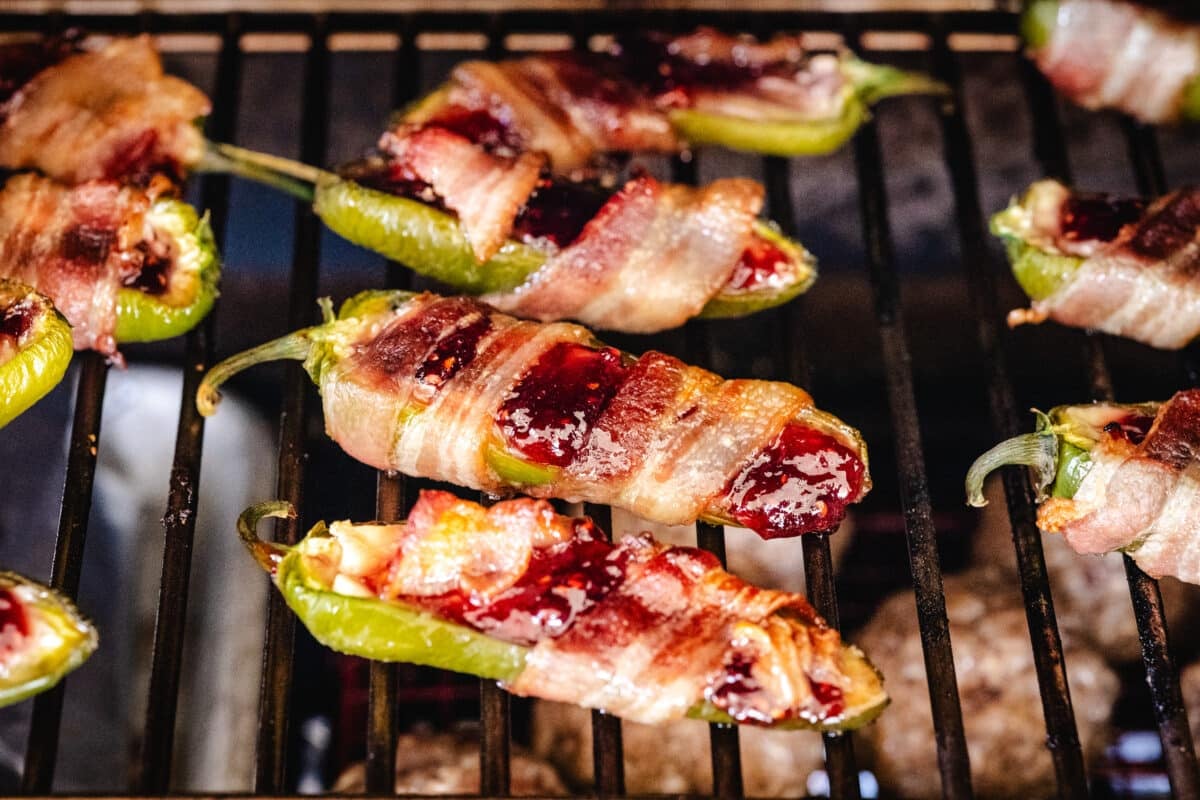Bacon wrapped jalapeño poppers on the grates of a smoker.