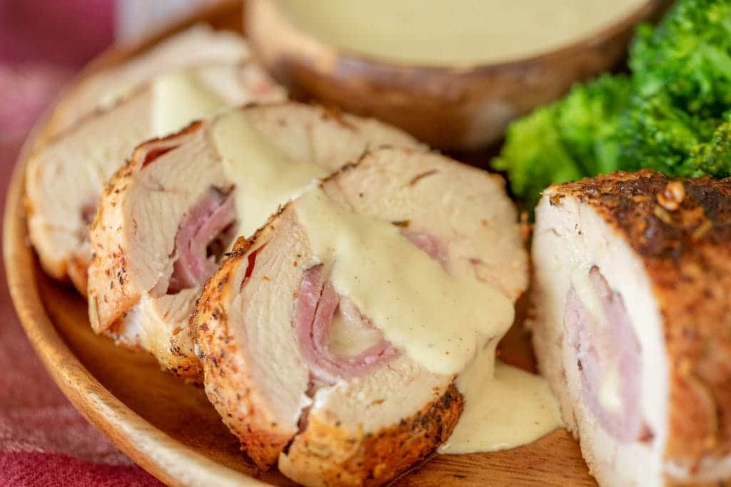 sliced chicken cordon bleu lined up in a wooden bowl drizzled with a white dipping sauce.