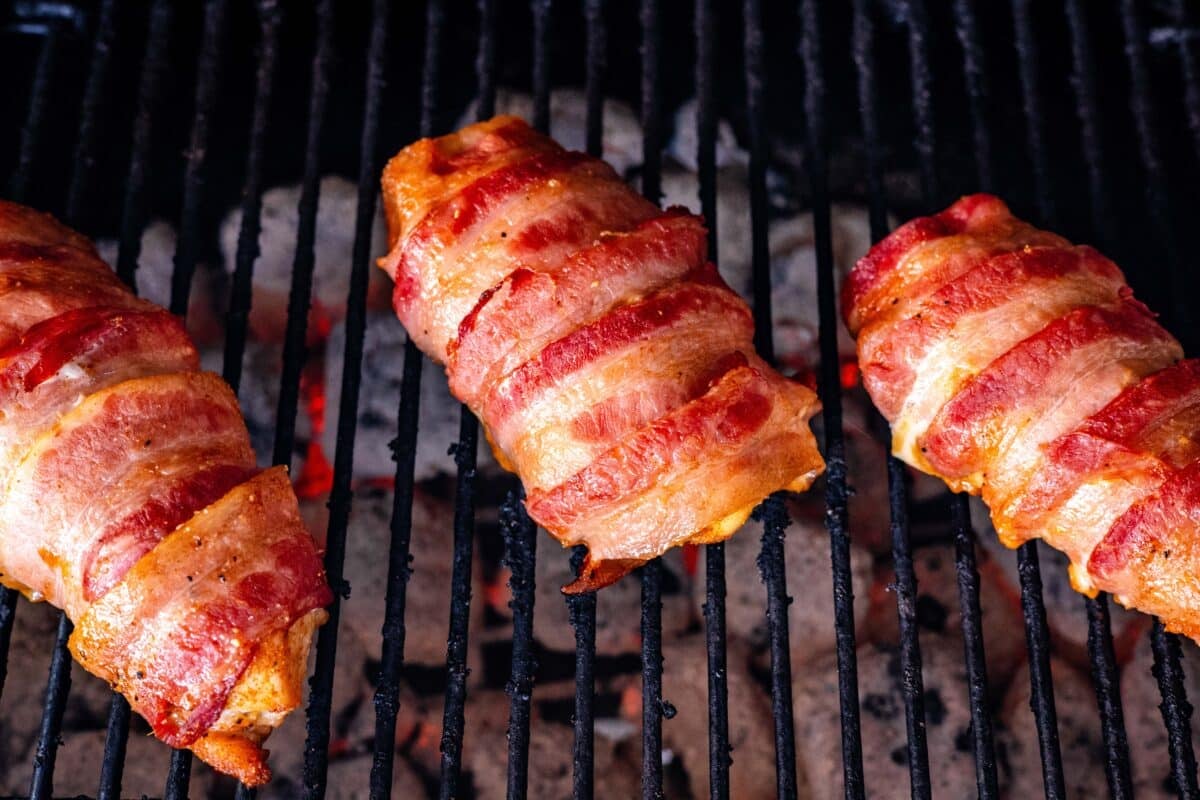 Poultry with a bacon weave on the grates of a smoker.