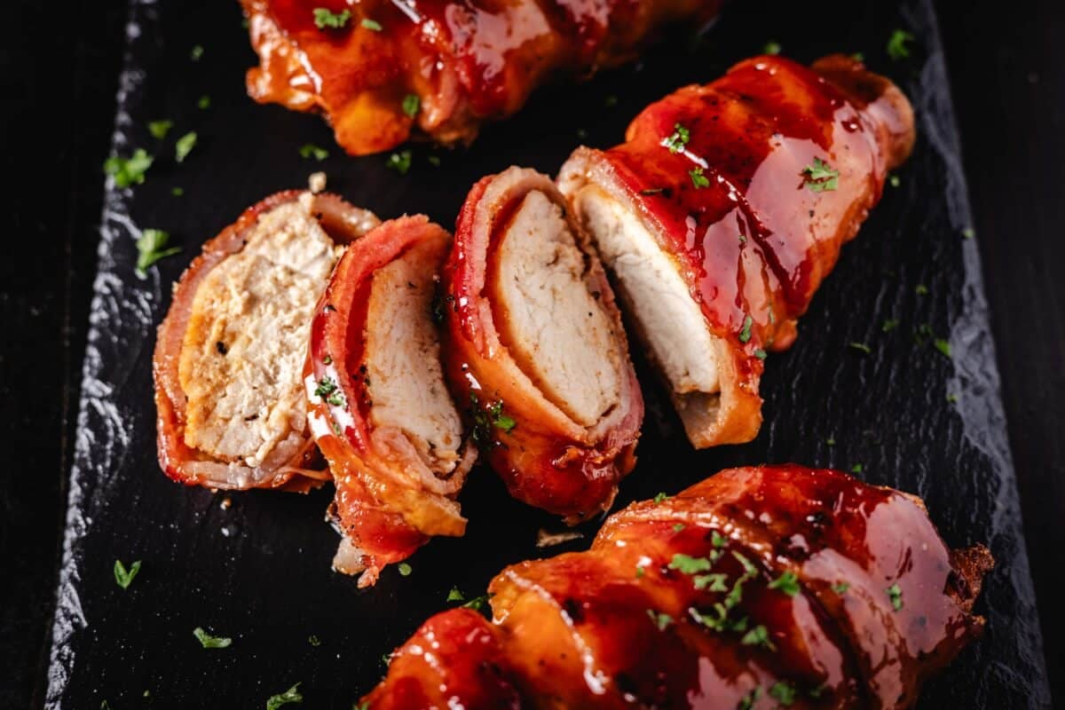 Three bacon wrapped chicken breasts on a platter, with the middle one sliced.