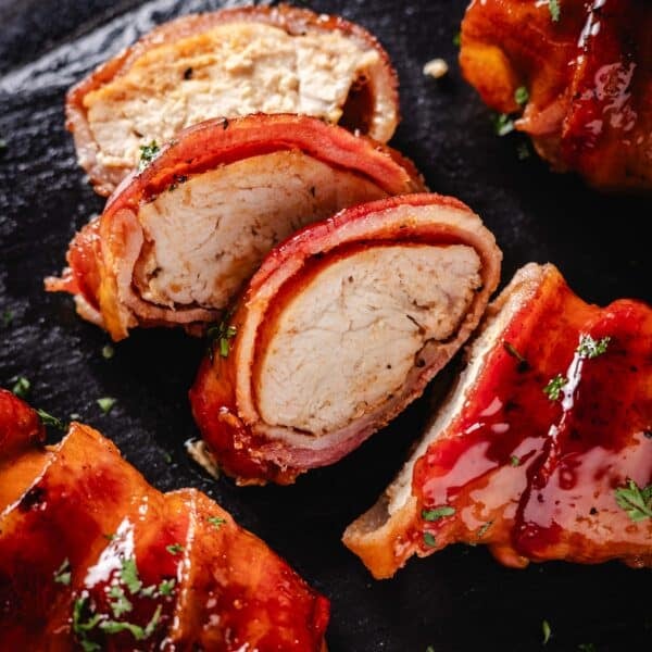 Grilled and sliced, bacon-wrapped chicken on a black plate.