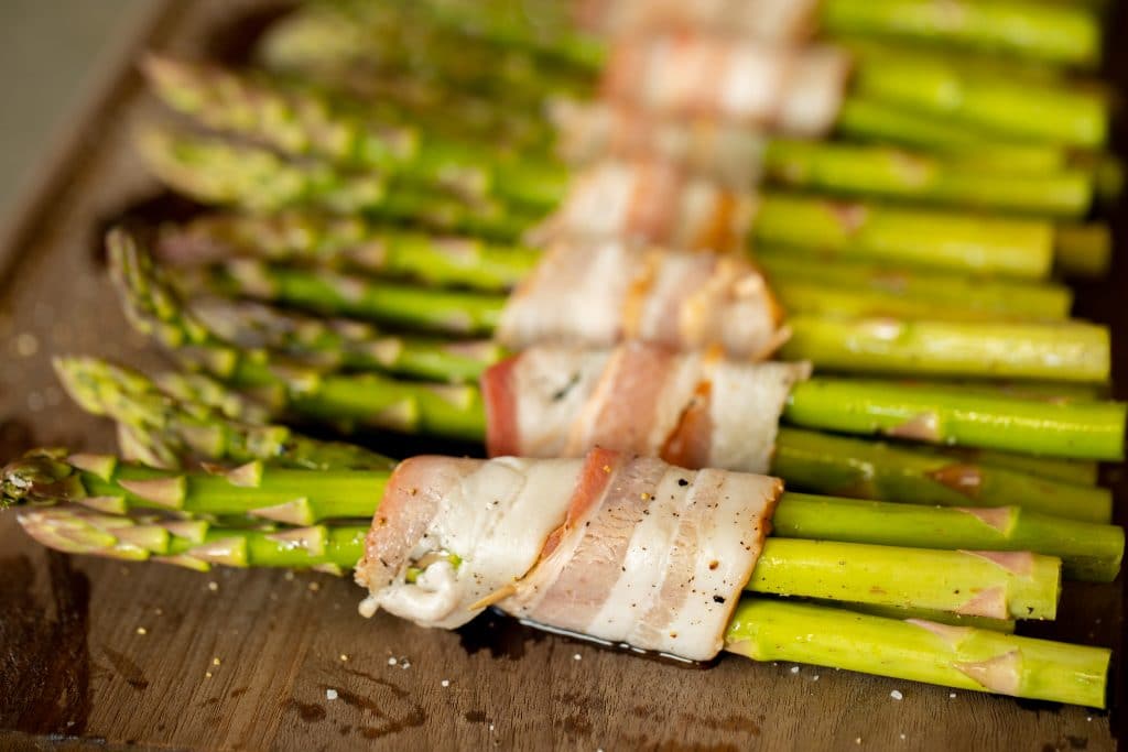 bacon wrapped asparagus bundles on a wooden cutting board