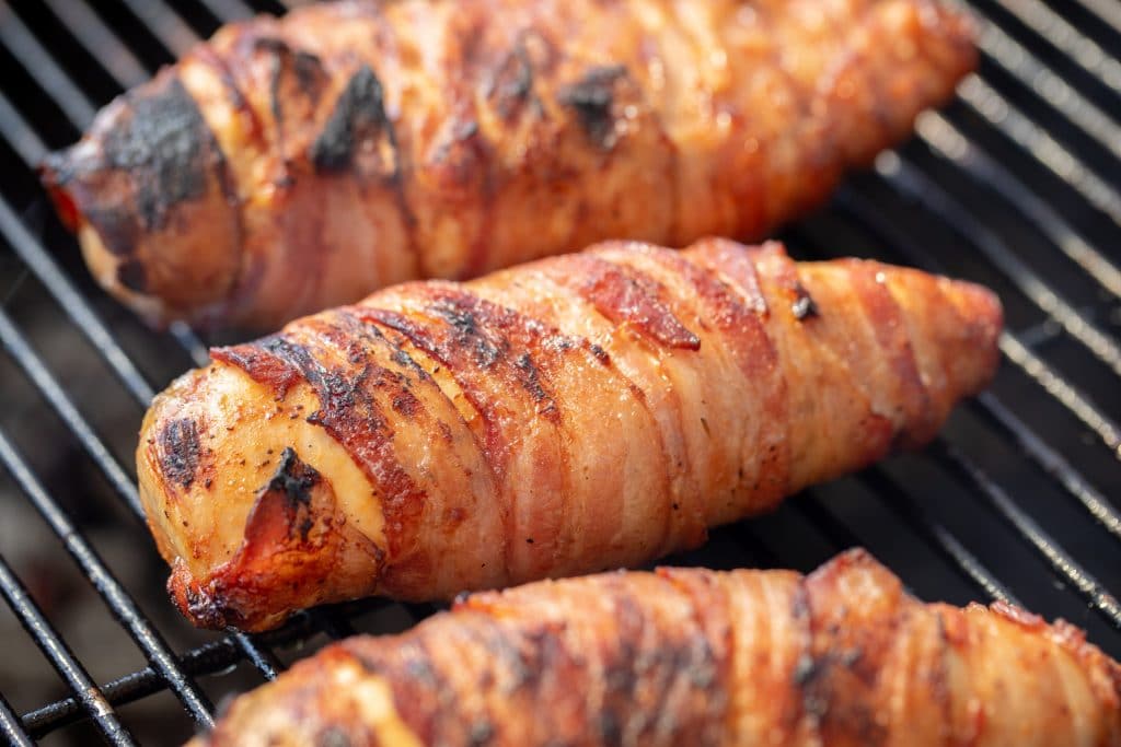 Three bacon wrapped chicken breasts on grill grates
