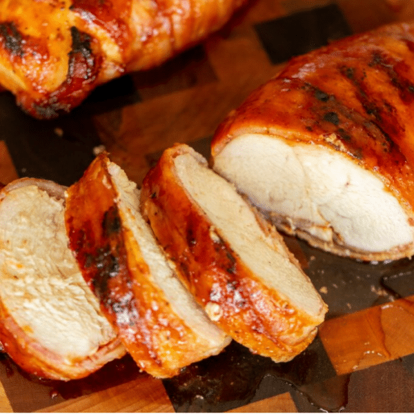 Sliced medallions of a bacon wrapped chicken breast on a wooden cutting board.