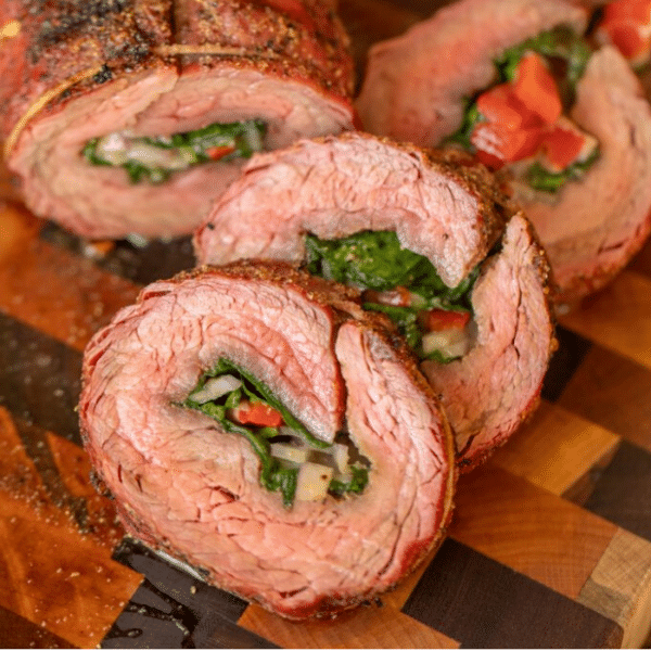 Cross section view of stuffed flank steak slices arranged on a wooden cutting board.