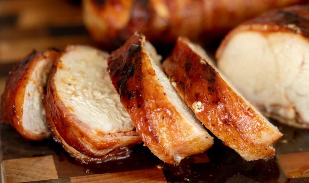 Eye level view of sliced bacon wrapped chicken breasts on a wood cutting board
