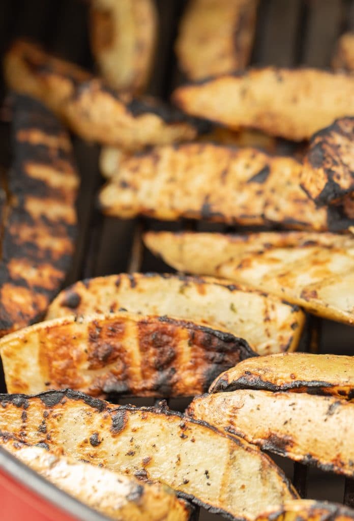 Close- up of grilled potato wedges on the grill grates of a charcoal grill.
