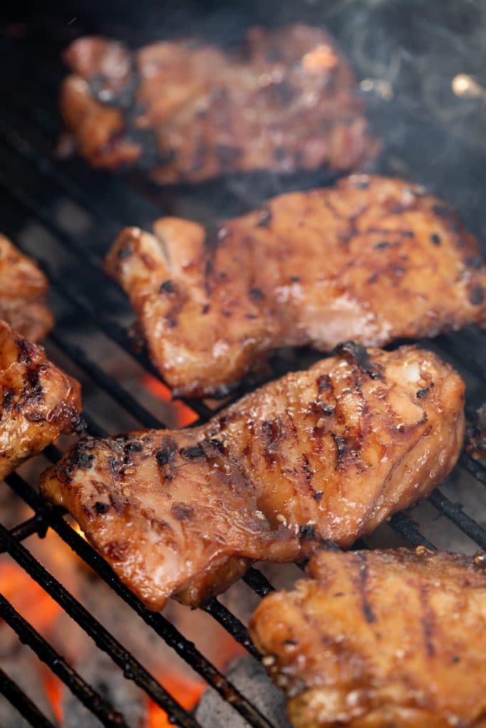 5 teriyaki chicken thighs on grill grates with hot charcoal directly underneath