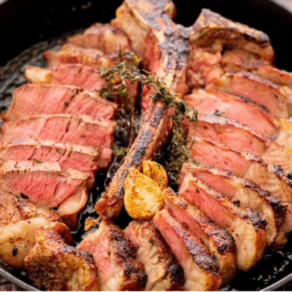 Sliced porterhouse steak in a cast iron skillet garnished with garlic cloves and thyme sprigs.