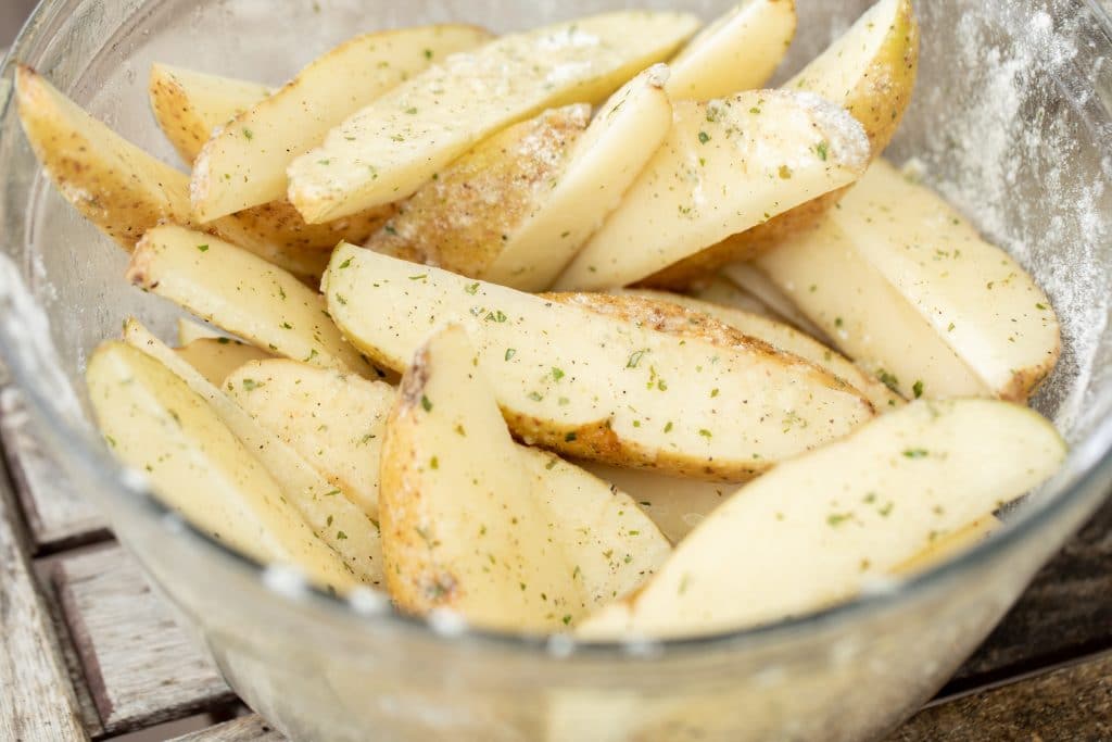 Raw potato spears covered in ranch seasoning and butter in a glass bowl.