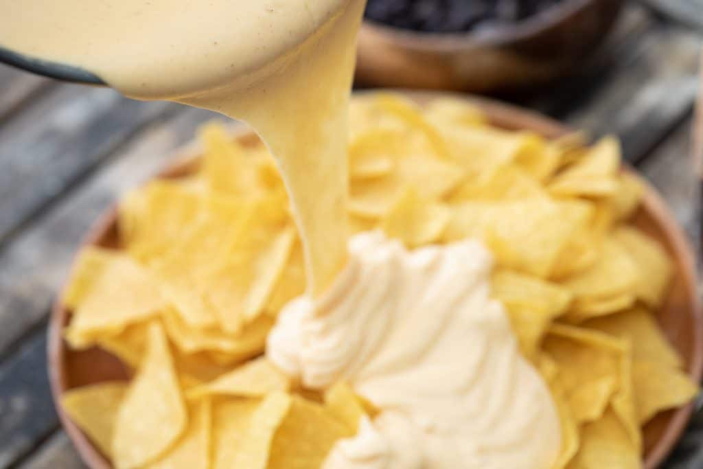 Nacho cheese sauce being poured from a pan onto a pile of tortilla chips.