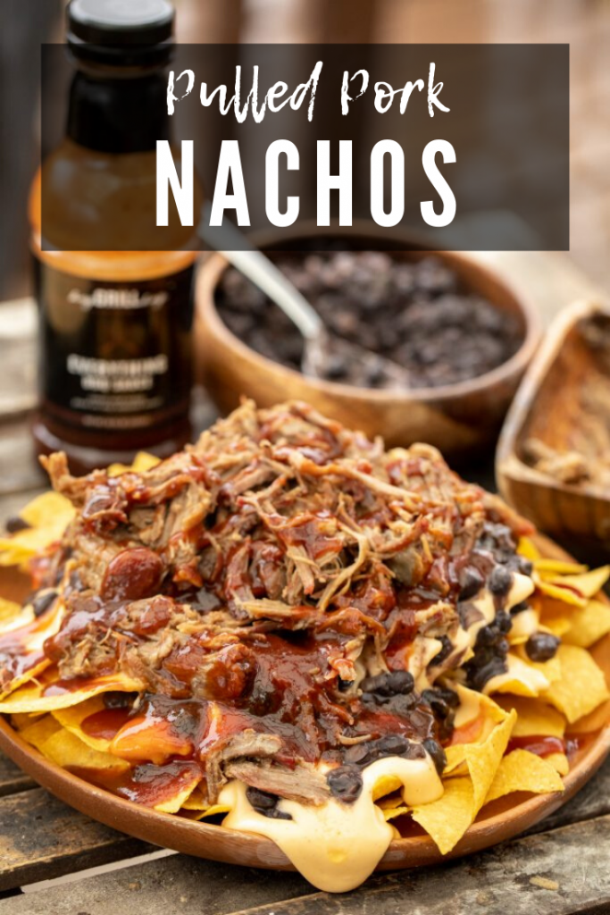 Pulled pork, bbq sauce, black beans, and cheese sauce layered on top of tortilla chips on a wooden plate with bottle of BBQ sauce and bowl of extra black beans in the background with decorative text.