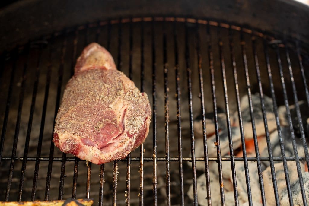 Seasoned steak on grill grates with hot coals underneath the opposite side of the grates.