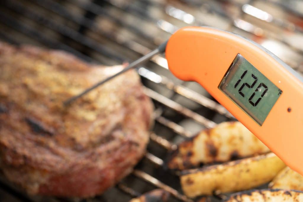 Orange thermometer reading a temperature of 120 degrees F inside of a steak.