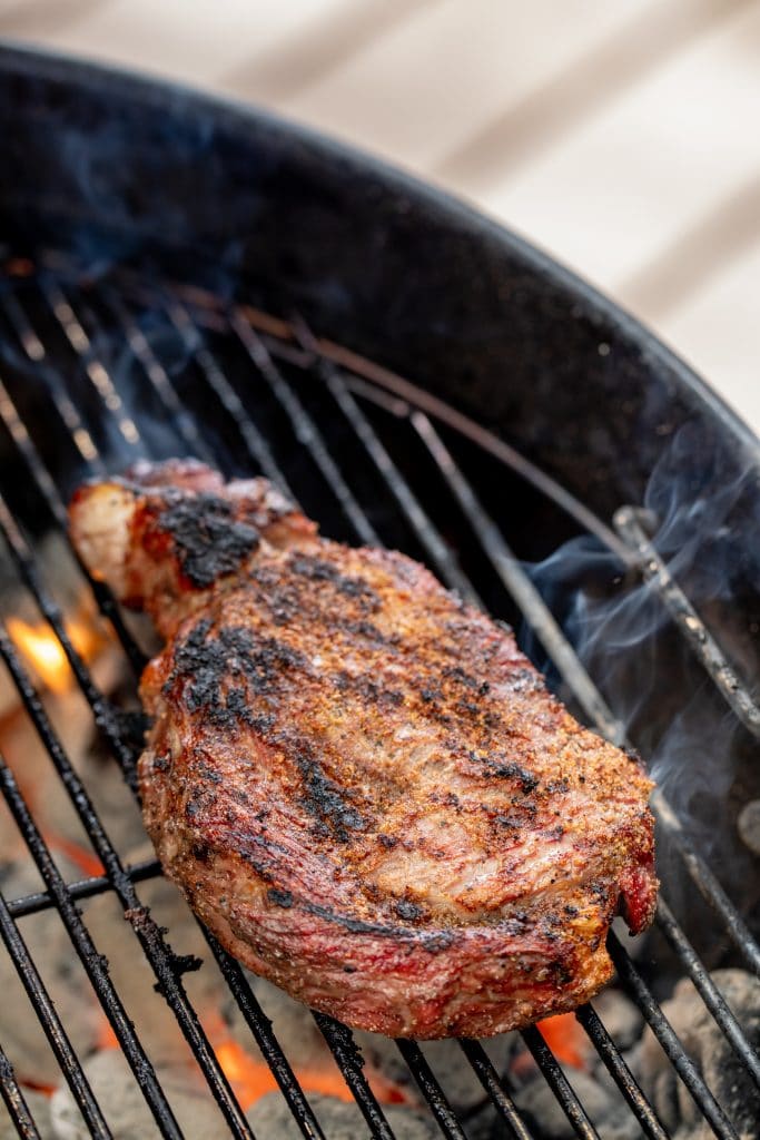 Steak searing on a grill grate over hot coals.
