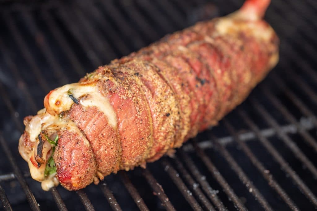 Stuffed flank steak starting to brown sitting on grill grates.