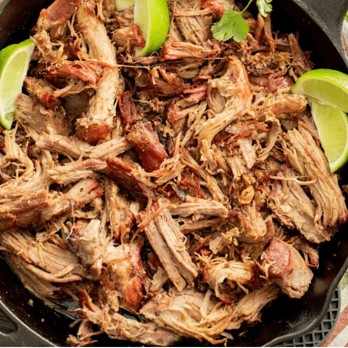 Shredded smoked pork carnitas in a cast iron skillet garnished with lime wedges.