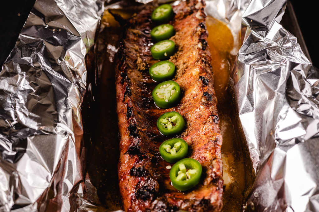 Ribs in foil covered in jalapeno slices.