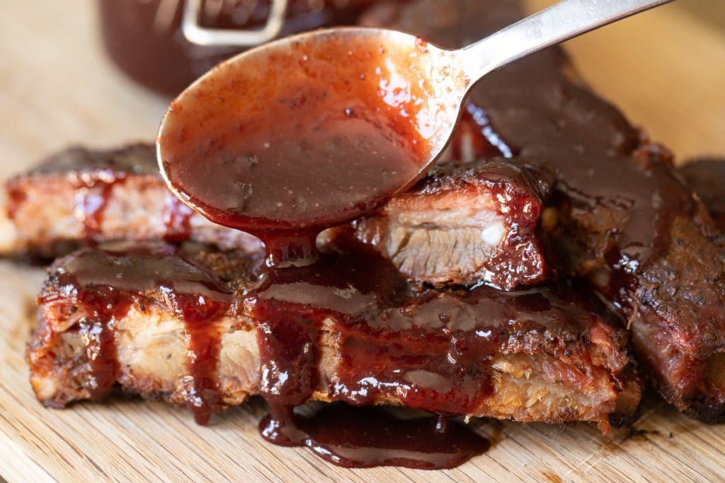 Spoonful of cherry cola BBQ sauce being drizzled over smoked ribs.