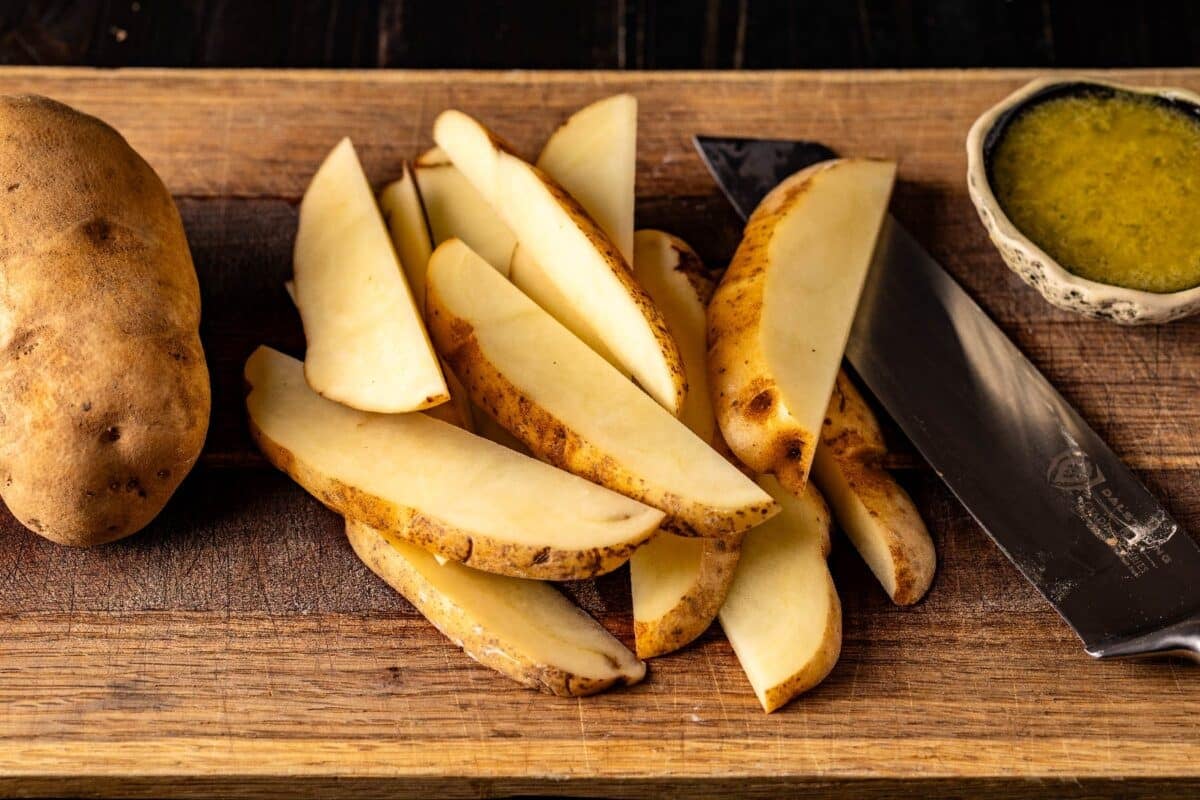 Potato spears on cutting board with knife and bowl of melted butter.