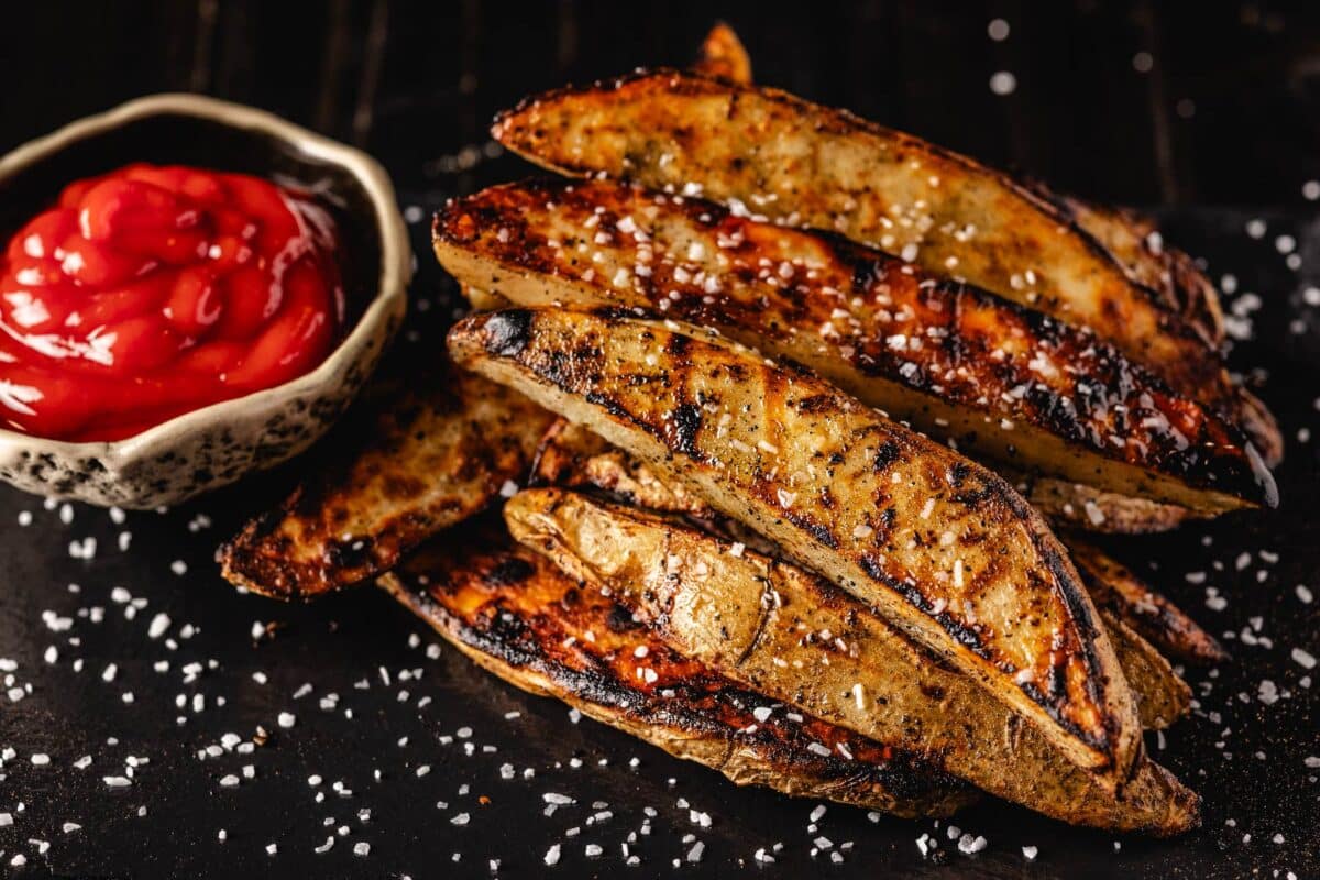 Grilled potato slices on serving platter with bowl of ketchup.