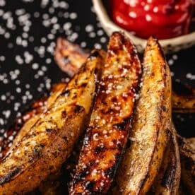 Potato wedges on serving platter with salt sprinkles and a bowl with ketchup.