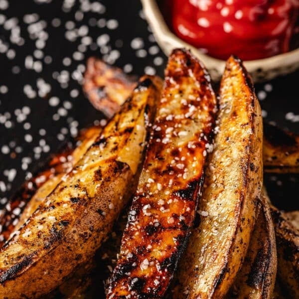 Potato wedges on serving platter with salt sprinkles and a bowl with ketchup.