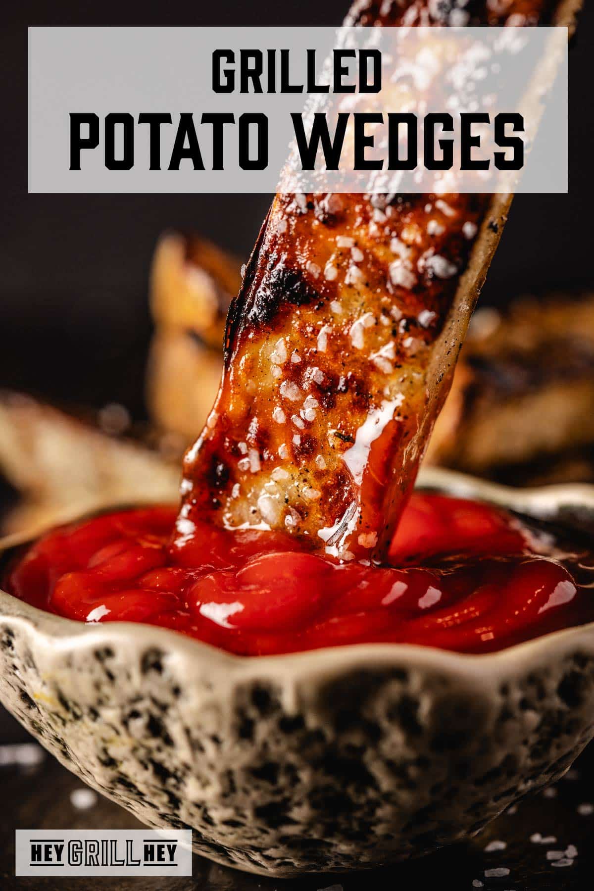 Salted potato wedge dipping into bowl of ketchup. Text reads "Grilled Potato Wedges."