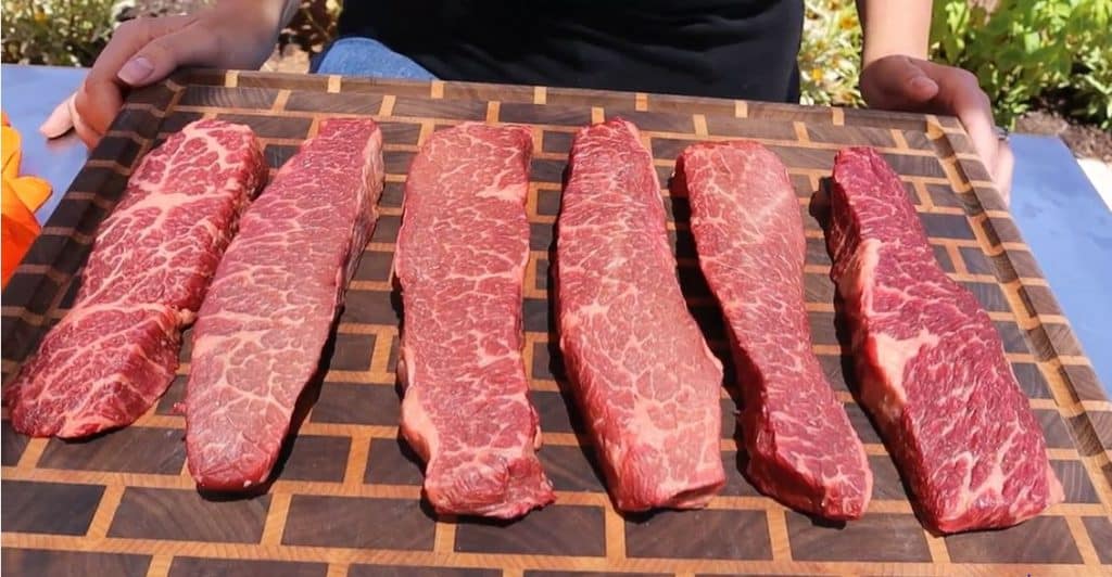 Six raw boneless beef short ribs lined up on a wooden cutting board.