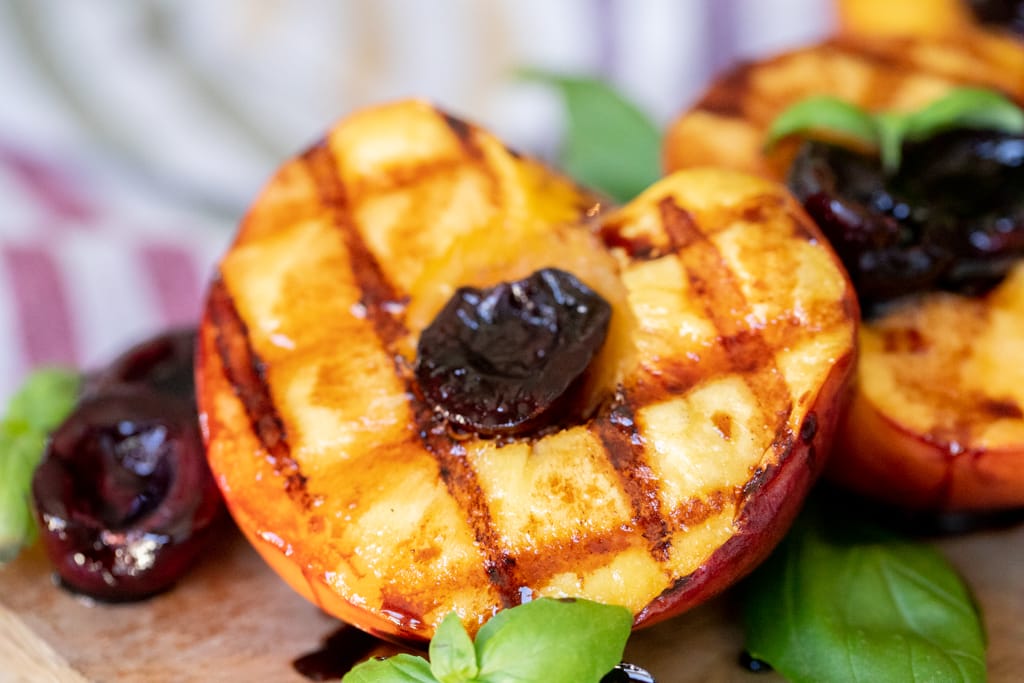 Grilled peaches with grill marks halved and glazed with cherries.