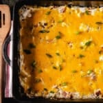 A cheese casserole in a cast iron pan next to a wooden spatula.