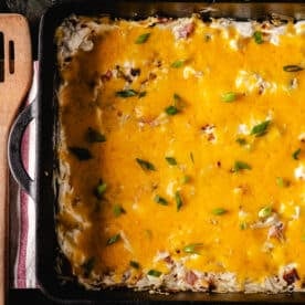 A cheese casserole in a cast iron pan next to a wooden spatula.
