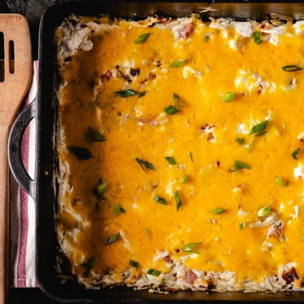 A cheese casserole in a cast iron pan next to a wooden spatula.