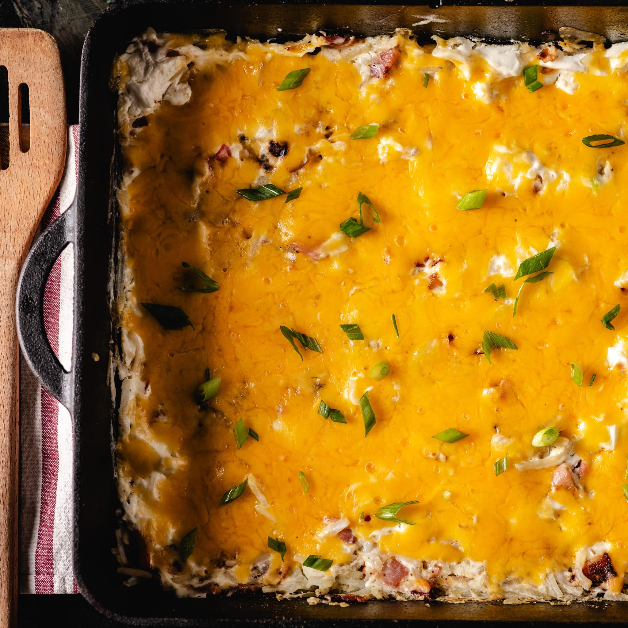 A cheese casserole in a cast iron pan next to a wooden spatula.