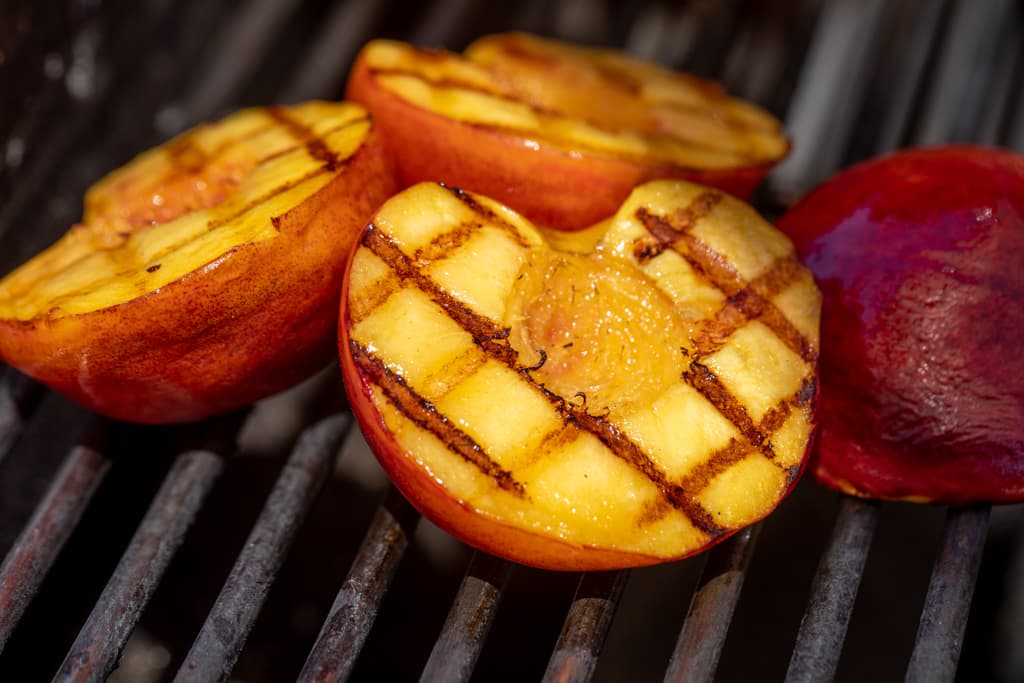 Grilled peaches halved on grill grates.