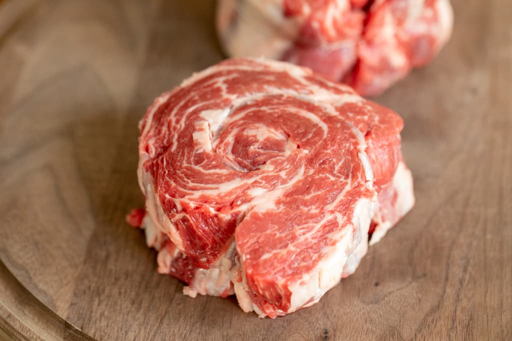 Raw Ribeye Cap Steak tied with butcher's twine, on a wood cutting board.
