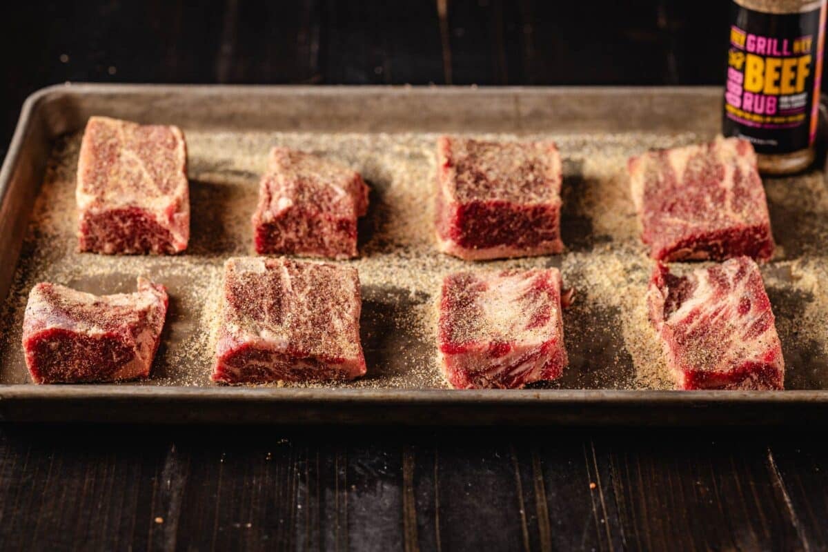 Sliced beef on baking sheet sprinkled with seasoning.