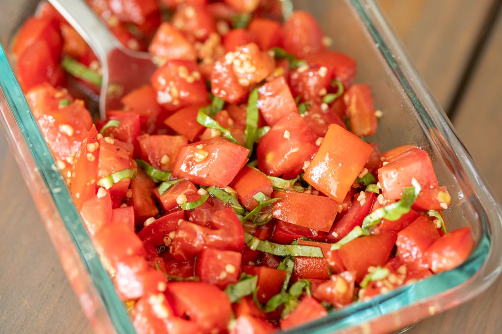 Diced tomatoes, shredded basil, and minced garlic in a glass dish.