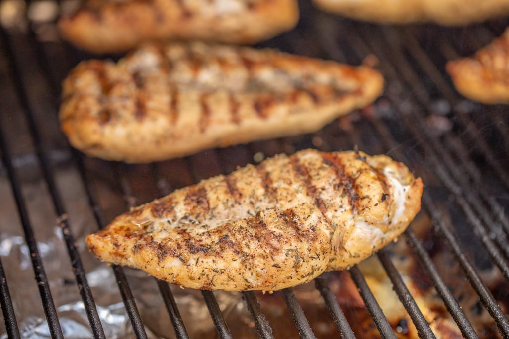 Seasoned chicken breast on grill grates with grill marks.