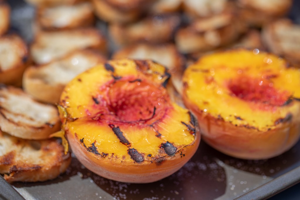 Two grilled peach halves on a metal baking sheet.