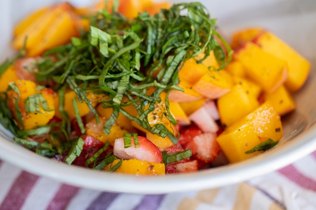 Bowl of diced peaches and strawberries topped with shredded basil.