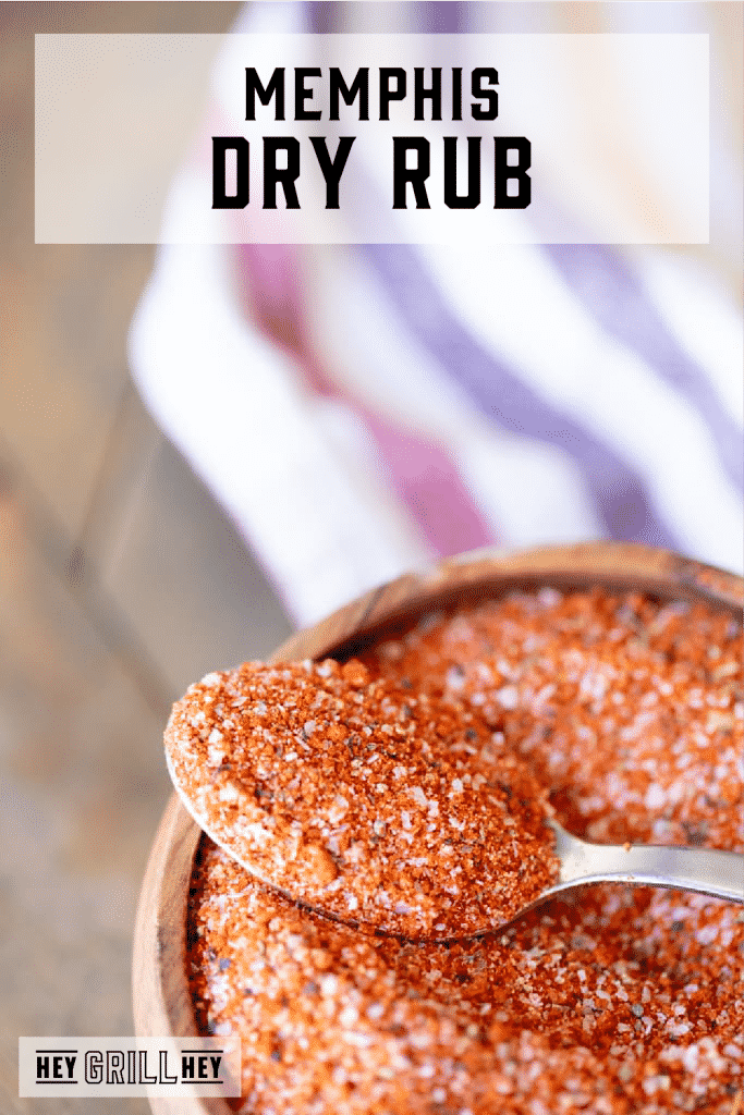 Spoonful of Memphis dry rub resting on top of a wooden bowl full of more seasoning with text overlay - Memphis Dry Rub.
