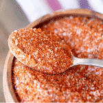 Spoonful of Memphis dry rub resting on top of a wooden bowl full of more seasoning.