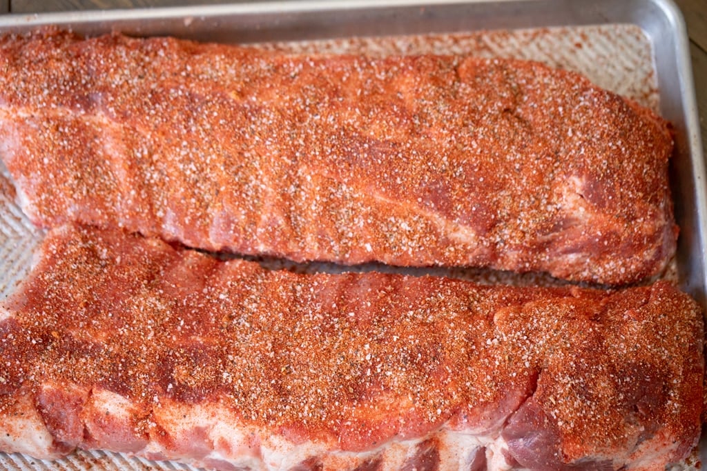 Overhead view of two racks of uncooked pork ribs seasoned with Memphis dry rub.