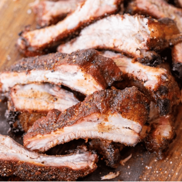 Sliced Memphis style dry rub ribs arranged in a pile on a wood cutting board.