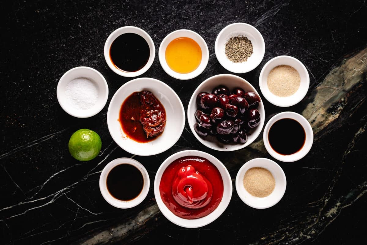 An overhead shot of several white bowls with liquids and seasonings sitting on a dark surface.