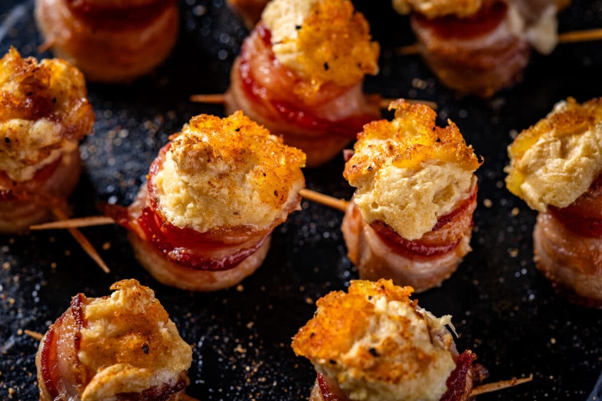 A closeup shot of pineapple cream cheese bacon shots on a black platter.