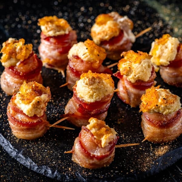 Several bacon-wrapped cream cheese balls on a black platter.