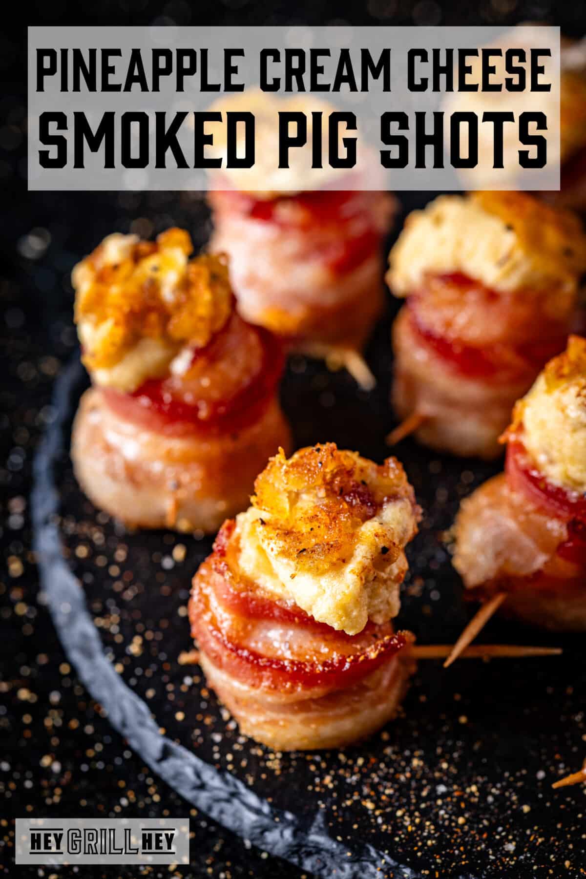 A closeup shot of cream cheese pig shots on a black plate. The text overlay reads "Pineapple Cream Cheese Smoked Pig Shots" at the top, and "Hey Grill Hey" at the bottom.